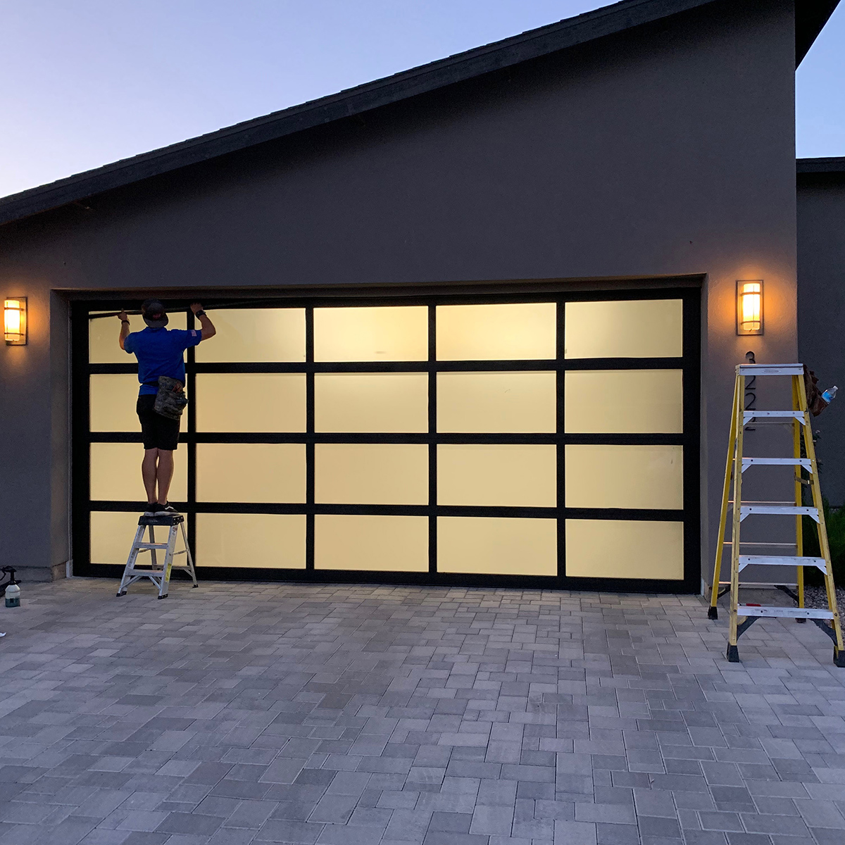 Garage door installer working on a modern glass and black frame garage door.