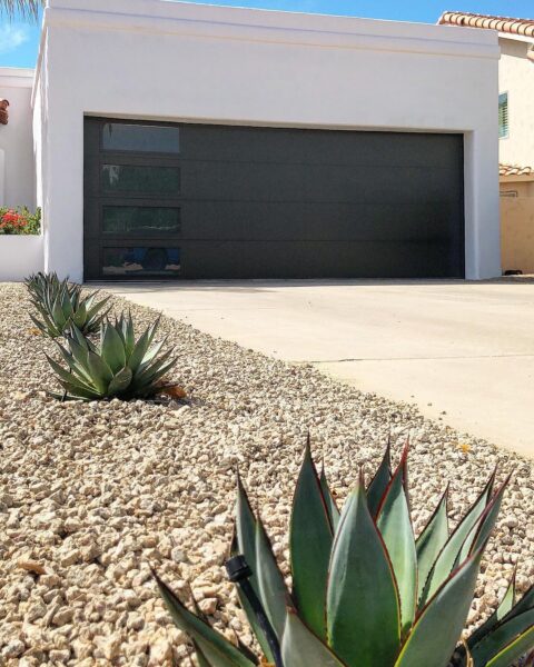 Contemporary Dark Garage Door with Horizontal Windows and Desert Landscaping Close-up photograph of a modern home featuring a dark gray, flush garage door with a row of three long, narrow, horizontal windows.