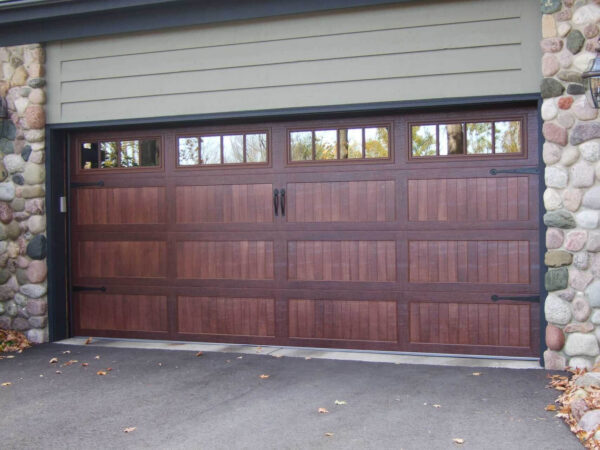 Elegant wood garage door with window panels installed on a stone-accented residential home.