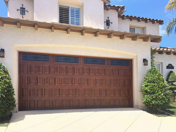 Wooden residential garage door installed on a modern stucco home in a suburban neighborhood