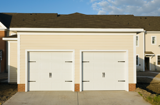 Residential home with two white garage doors, clean driveway, and neutral exterior siding.