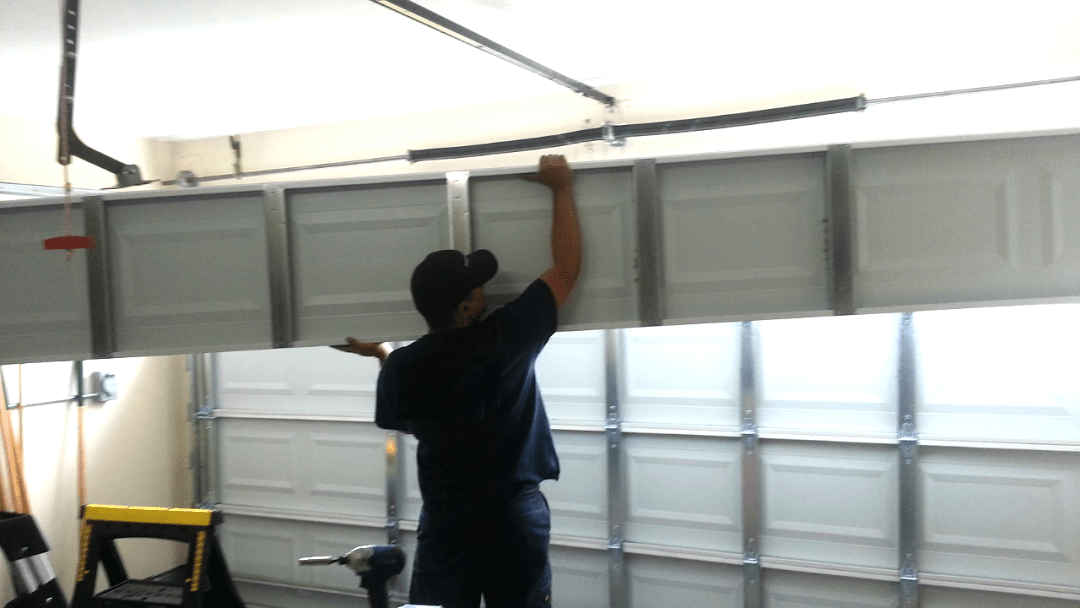 Technician adjusting and securing garage door panels inside a residential garage